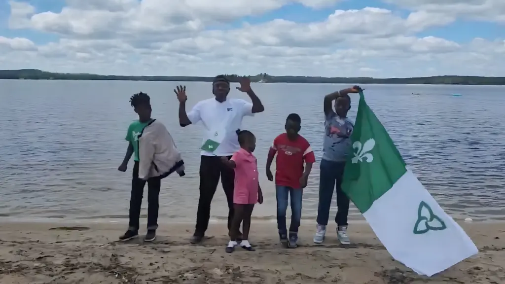 Un groupe de personnes et d'enfants sur une plage agitant un grand drapeau franco-ontarien.
