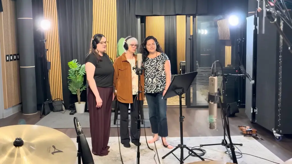 Trois femmes chantent ensemble devant un microphone dans un studio.