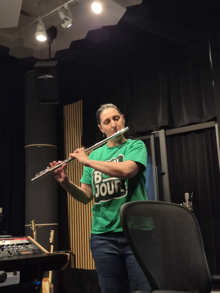 Une femme vêtue d'un chandail vert joue de la flûte traversière en studio.