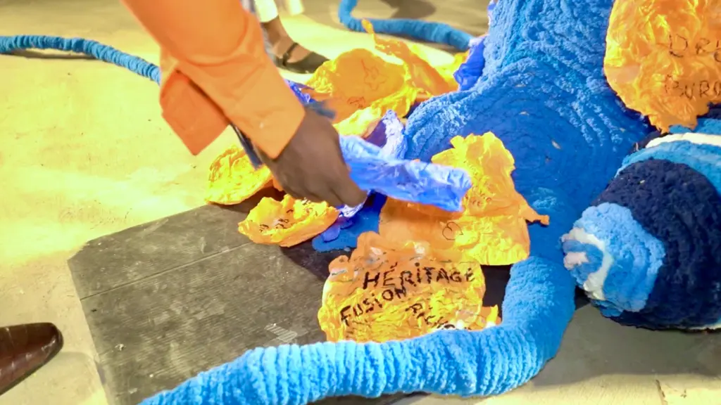Gros plan d'une main ajoutant des morceaux de papier orange portant les mots « HÉRITAGE » et « FUSION » sur une base sculptée bleue.