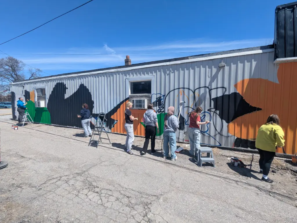 Students and an artist paint the first large blocks of colour on a white wall.
