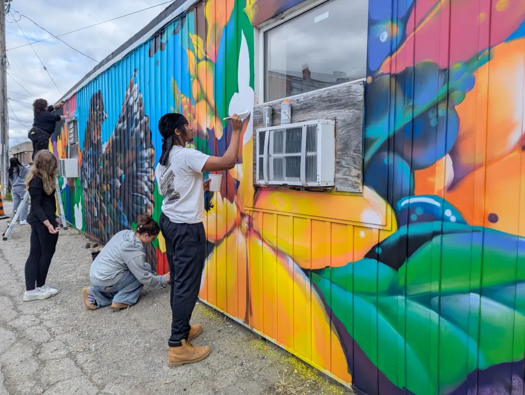 Two young people paint colourful yellow and green motifs around a window.