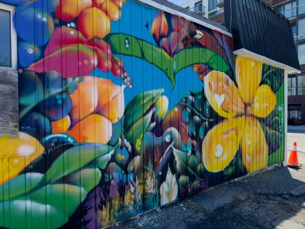 Detail of the mural showing large green leaves, stylized orange fruits, and a large yellow flower.
