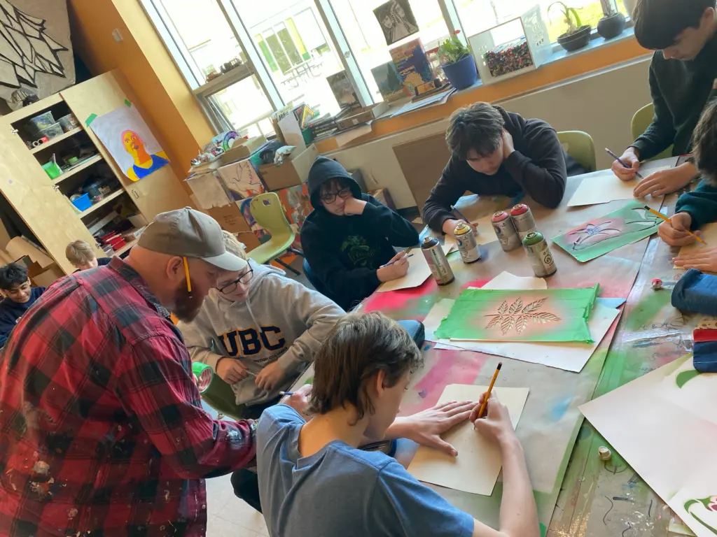 Un artiste en chemise à carreaux aide un jeune élève à dessiner sur son bureau.