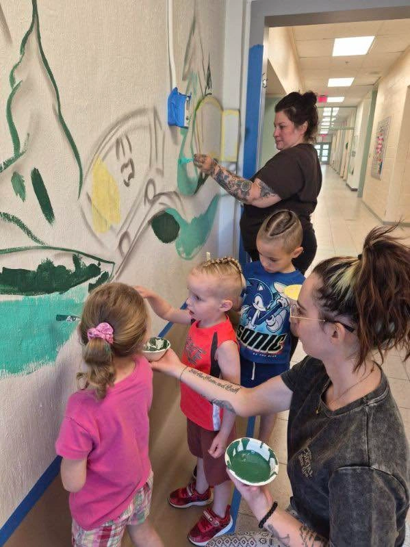 L'artiste Mique Michelle aide de très jeunes enfants à peindre un train en jaune sur le mur du corridor.