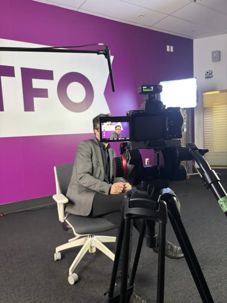 Un homme est interviewé et filmé devant un grand mur violet affichant le logo de TFO.