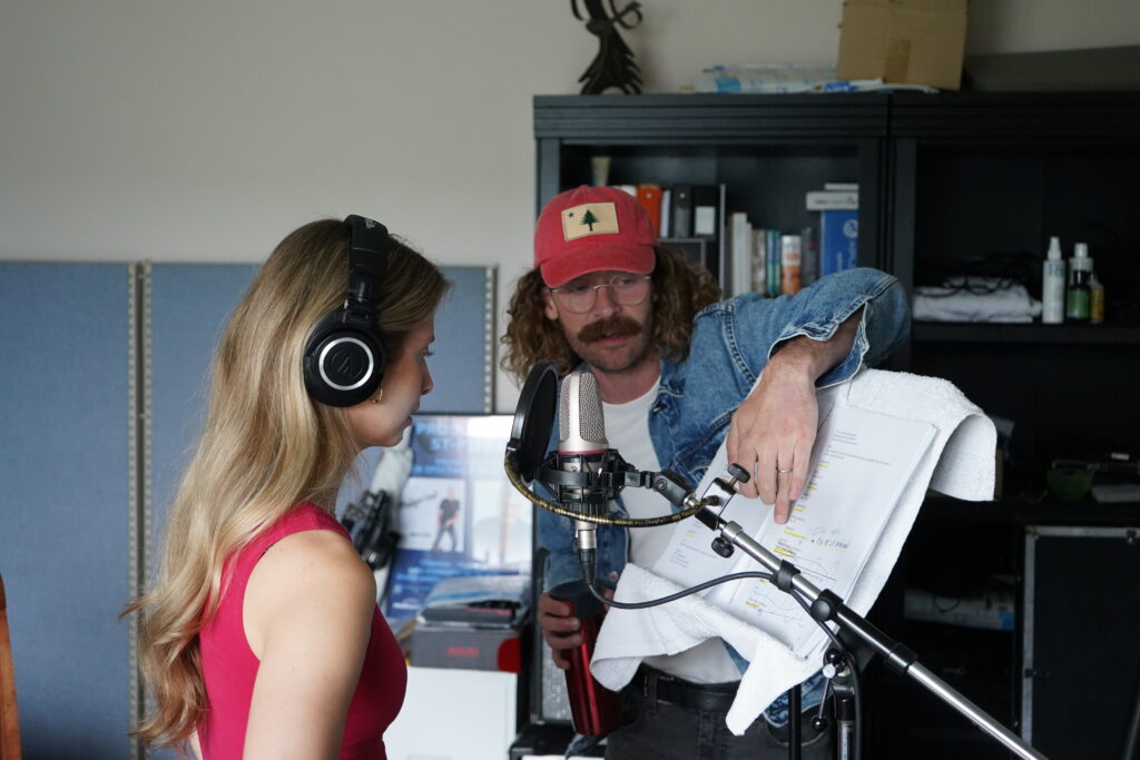 Une femme et un homme portant une casquette rouge examinent une partition ensemble en studio.