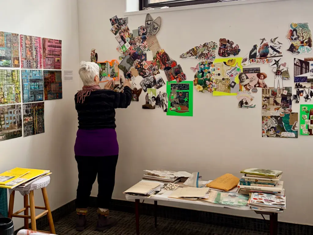 Personne debout devant un mur, installant des collages parmi plusieurs créations affichées.