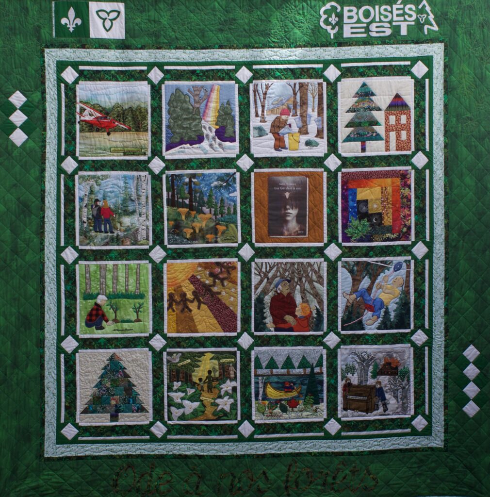Grande courtepointe collective verte réunissant seize carrés illustrés sur le thème de la forêt, disposés en quatre rangées, avec les symboles franco-ontariens et le logo de Boisés Est dans la partie supérieure.