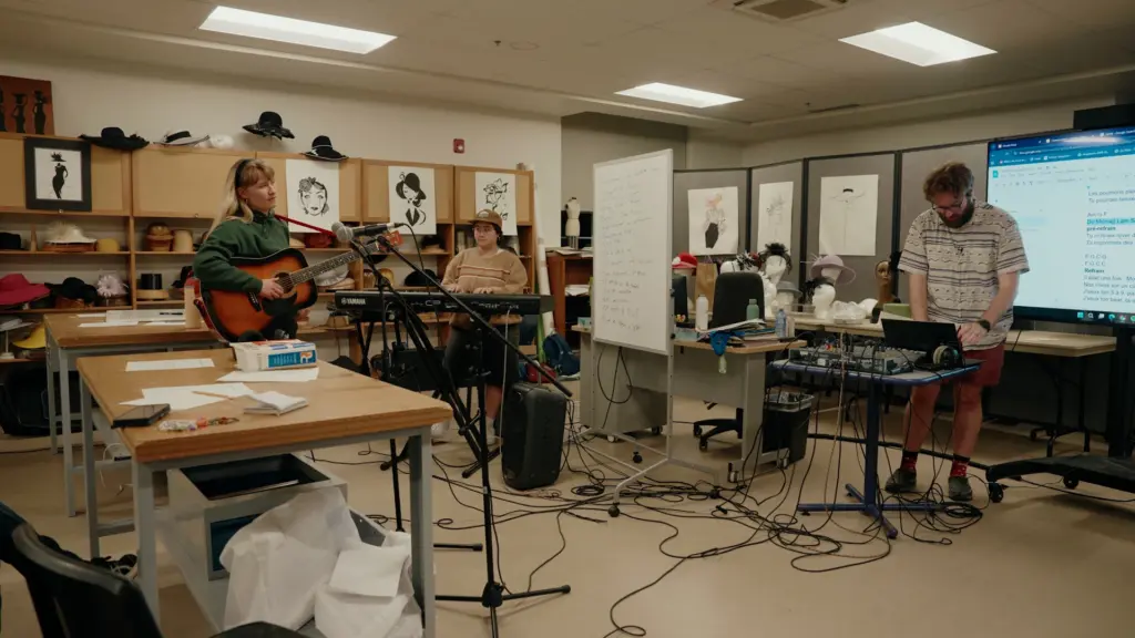 Une salle de classe transformée en studio avec des microphones, des câbles au sol, des instruments et des musiciens en répétition.