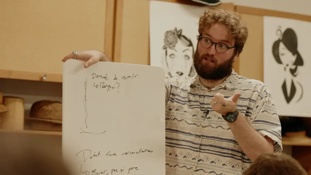 Un homme barbu portant des lunettes tient un petit tableau blanc avec des notes pour expliquer un concept à un groupe.