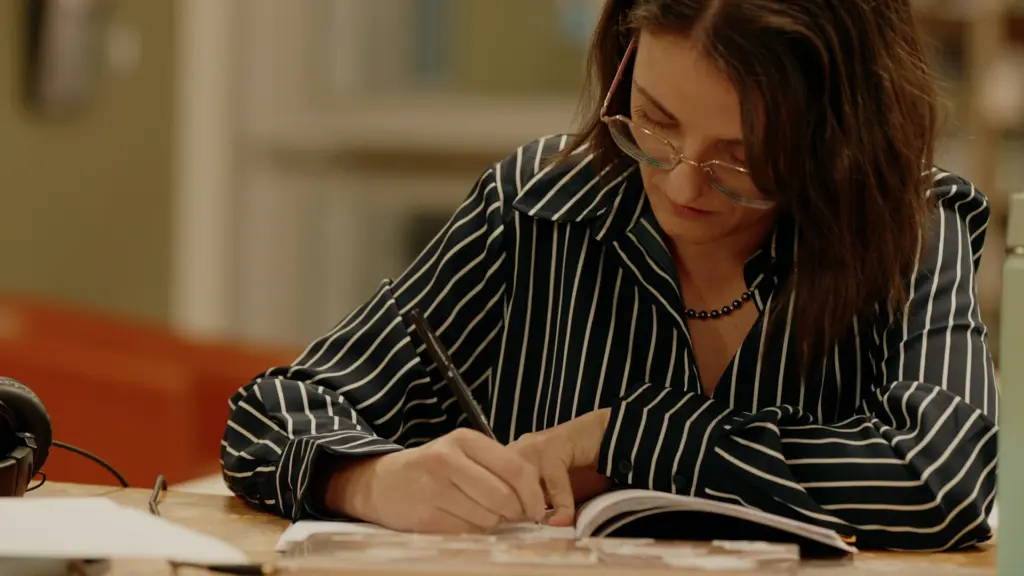 Une jeune femme portant des lunettes se concentre en écrivant attentivement dans son cahier de notes.
