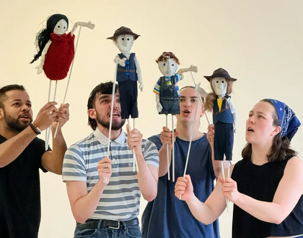 Quatre jeunes artistes tiennent des marionnettes à tige représentant différents personnages au-dessus de leurs têtes.