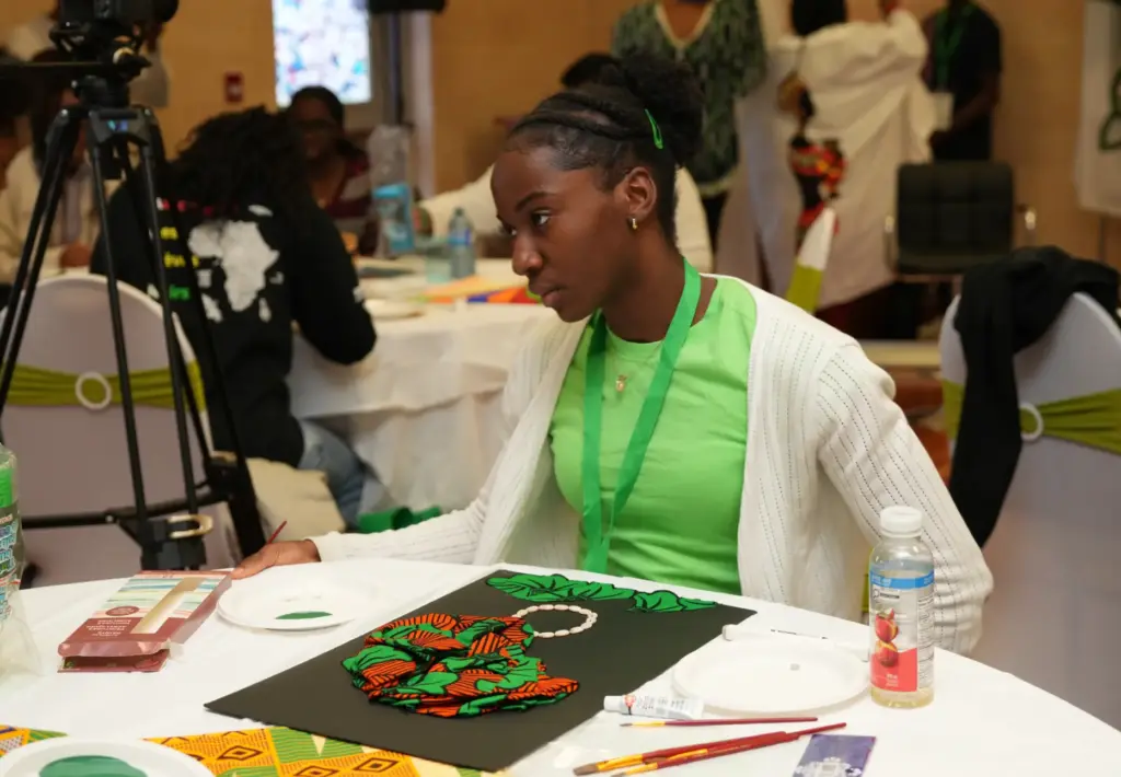 Une jeune femme assise à une table créant attentivement un collage artistique sur fond noir lors d'un atelier communautaire.