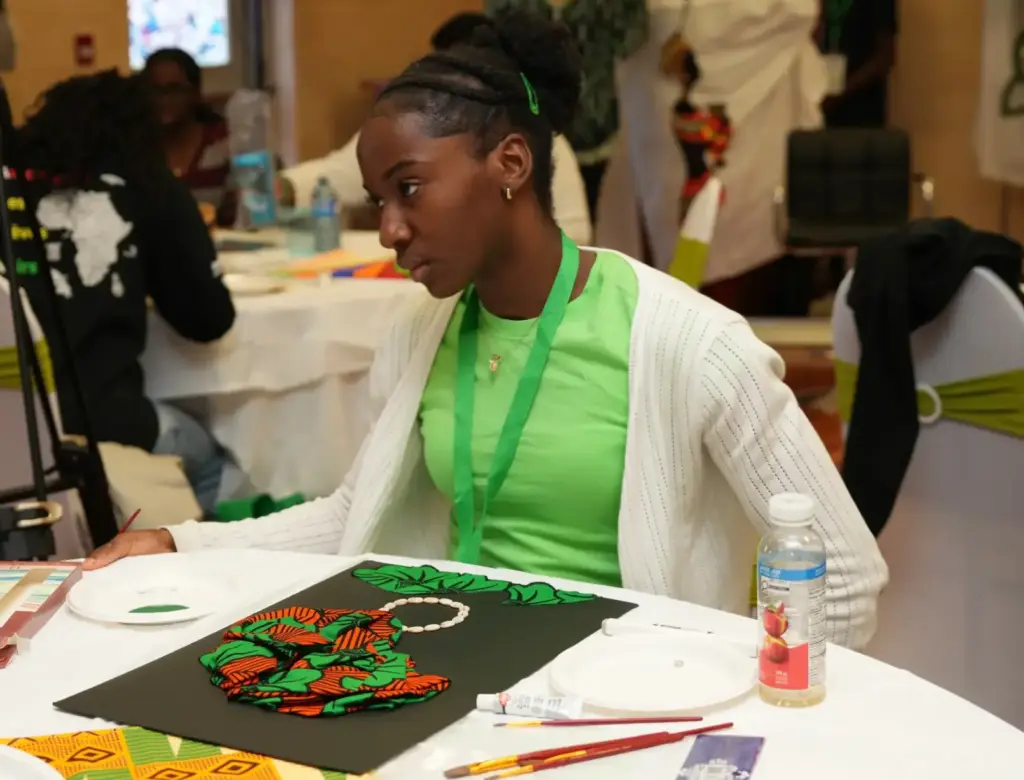 A young woman seated at a table carefully creates an art collage on a black background during a community workshop.