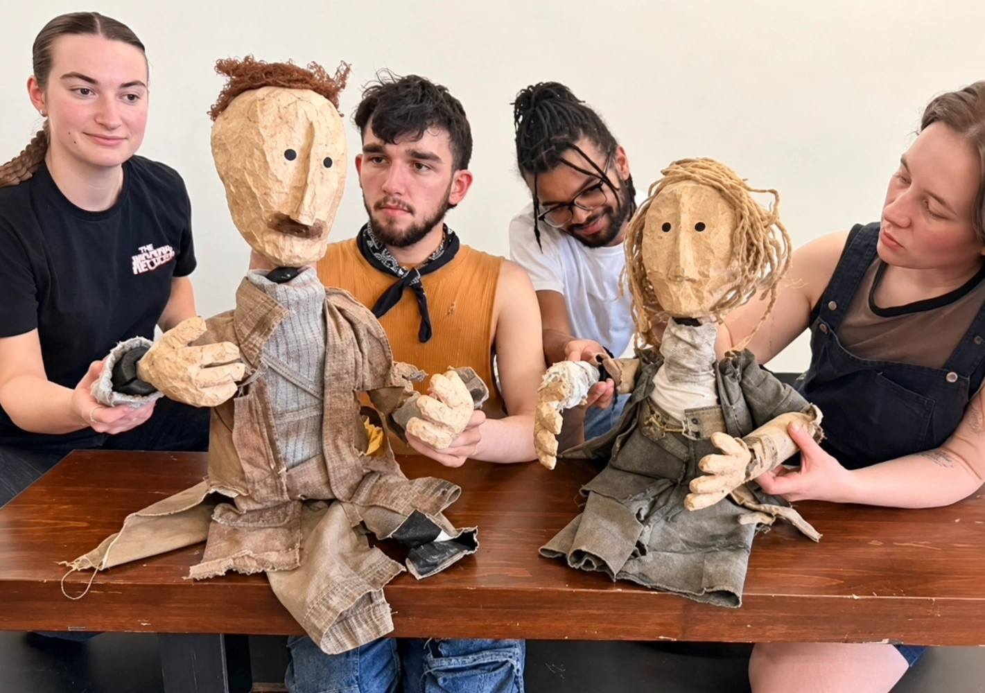 Quatre artistes posent autour de deux marionnettes en bois dans un espace de répétition.