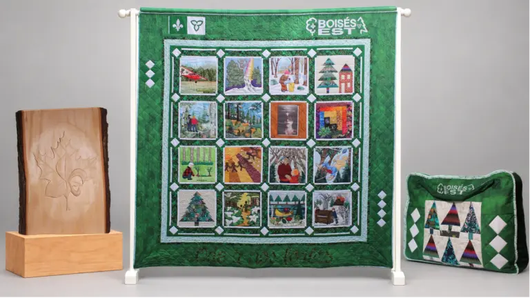 Trois créations sont présentées ensemble : une courtepointe verte composée de seize scènes liées à la forêt, une sculpture sur bois ornée d’une feuille d’érable et d’une fleur de lys, et une housse textile verte décorée de motifs d’arbres.