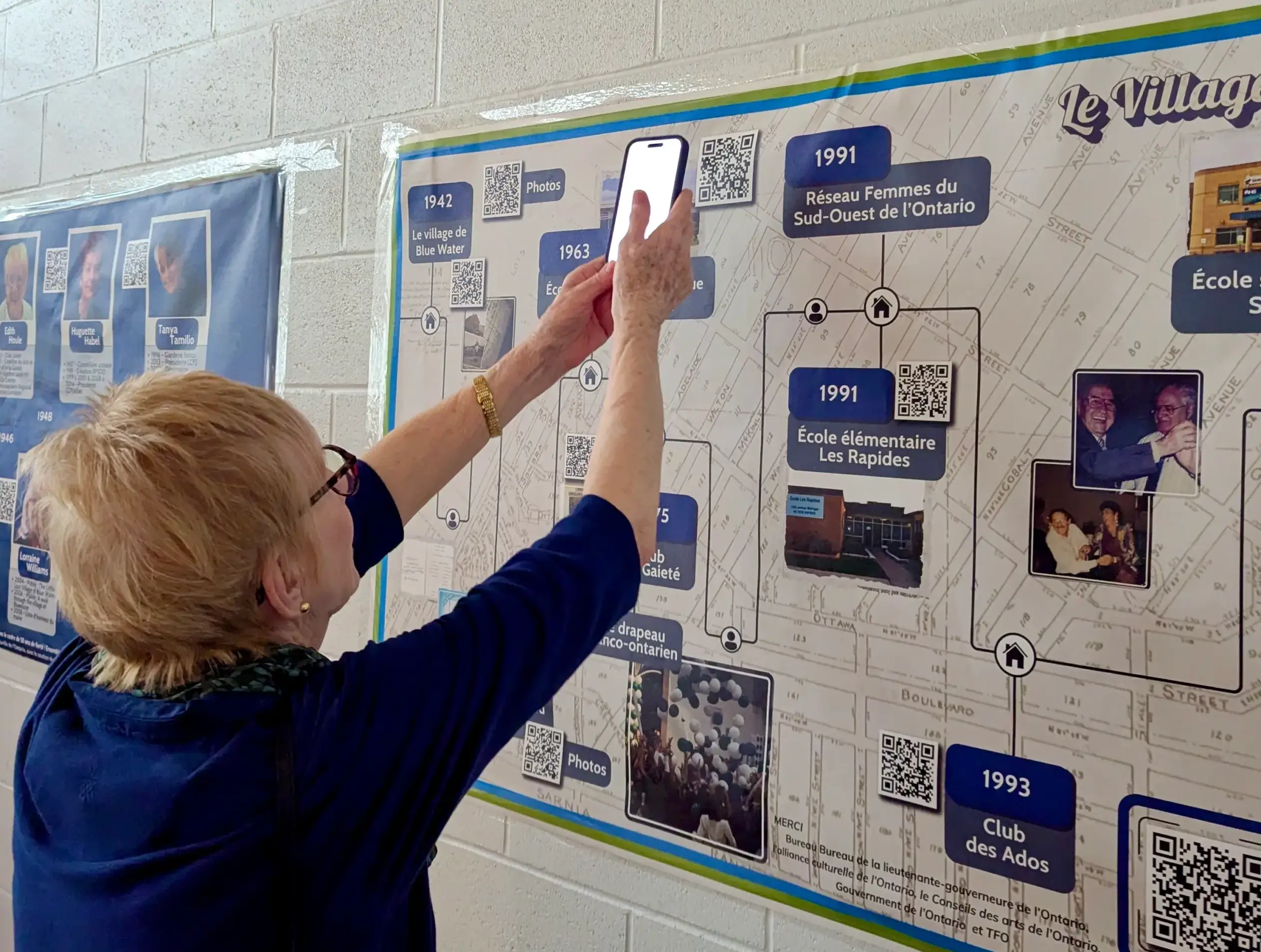 A visitor scans one of the QR codes integrated into the Racines, Résilience, Rayonnement panels, providing access to interviews and additional photographs.