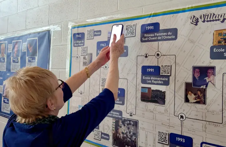 Une visiteuse consulte l’un des codes QR intégrés aux panneaux de Racines, Résilience, Rayonnement, qui donnent accès à des entrevues et à des photographies complémentaires.
