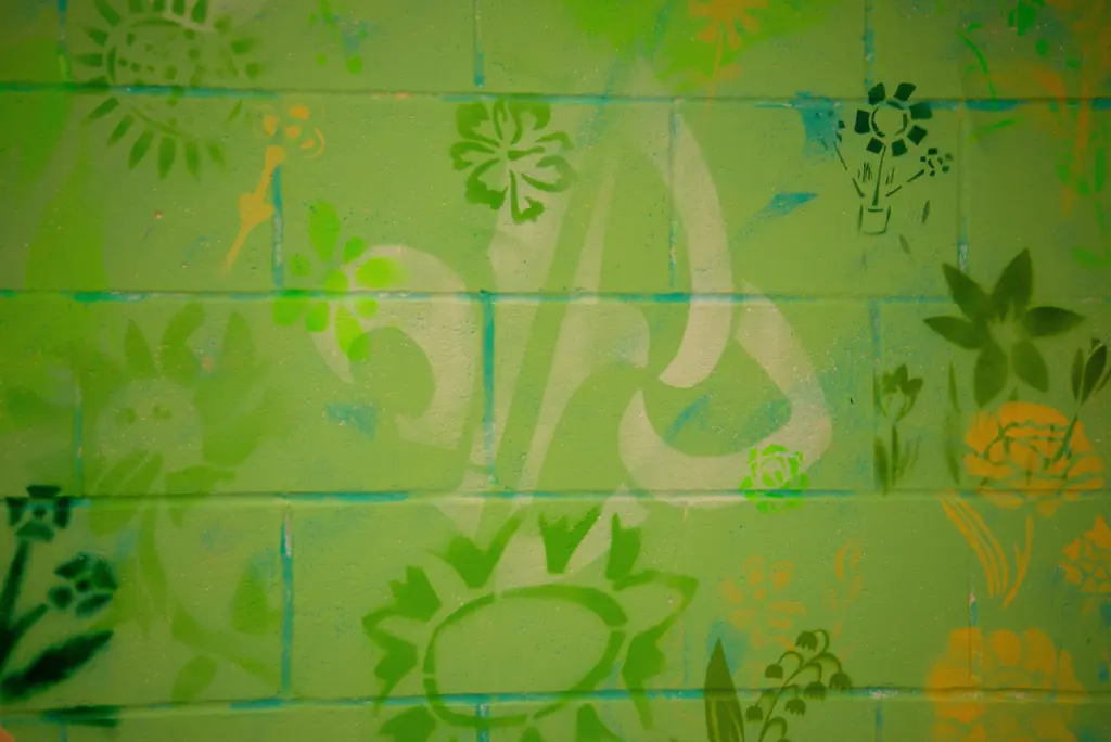 Gros plan d'une fleur de lys stylisée et de motifs organiques peints au pochoir sur un mur vert.