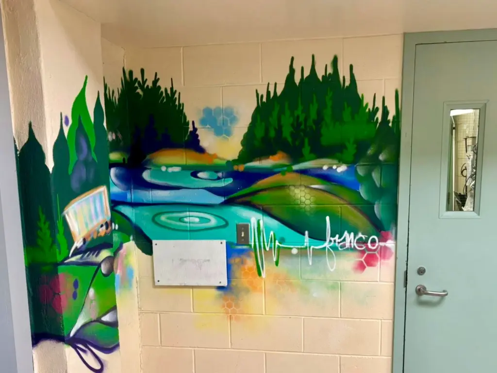 Section d’une murale intérieure représentant un paysage de forêt et de cours d’eau aux tons verts, bleus et turquoise, avec du matériel audio stylisé et une ligne évoquant une onde sonore suivie du mot « Franco ».