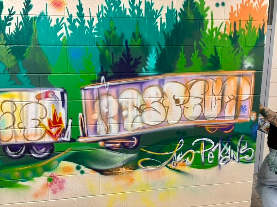 Section d’une murale intérieure montrant deux wagons de train portant le mot « RESPECT » en grandes lettres stylisées, devant une végétation verte et turquoise.
